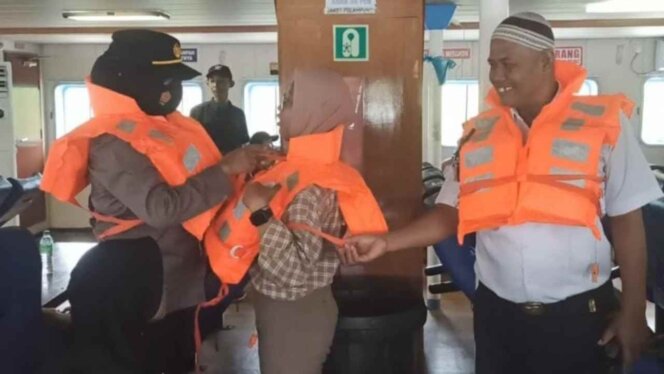 
					Kapolsek KKP Tanjungpinang mengenakan life jacket ke penumpang kapal. Foto: Istimewa
