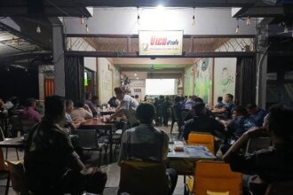 Babinsa Koramil 04/Dabo, Kodim 0315/TPI, Serda Darmadi, terlihat duduk di antara warga dengan mengenakan seragam lapangan TNI.